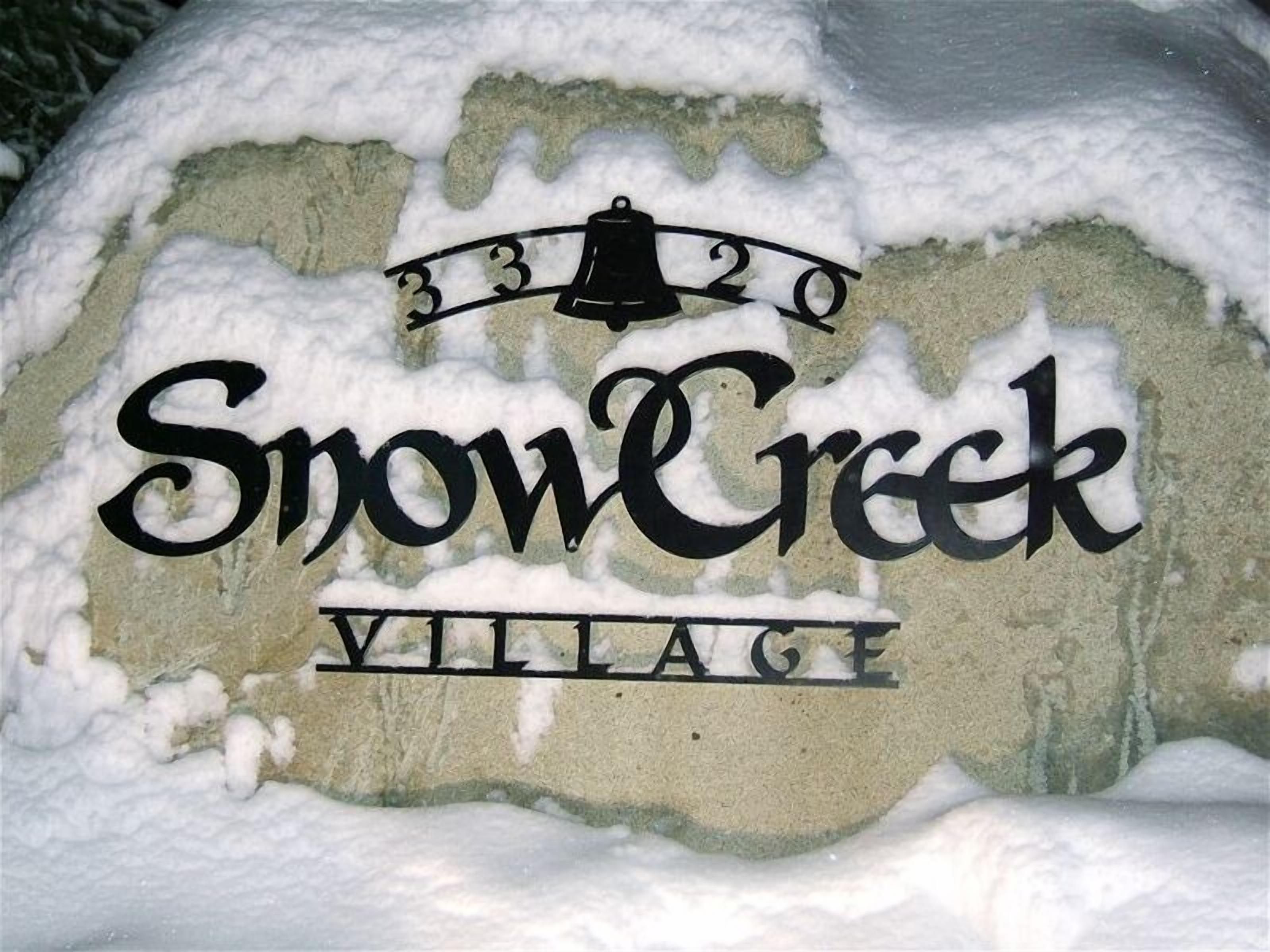 Et snedækket skilt med teksten "Snow Creek Village" og et klokkeikon over nummeret "3320".