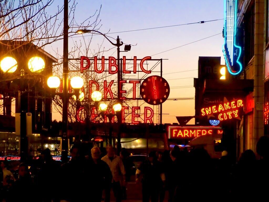 Une rue animée, avec des enseignes lumineuses, dont les panneaux « MARCHÉ PUBLIC » et « VILLE DES CHAUSSURES DE SPORT ».