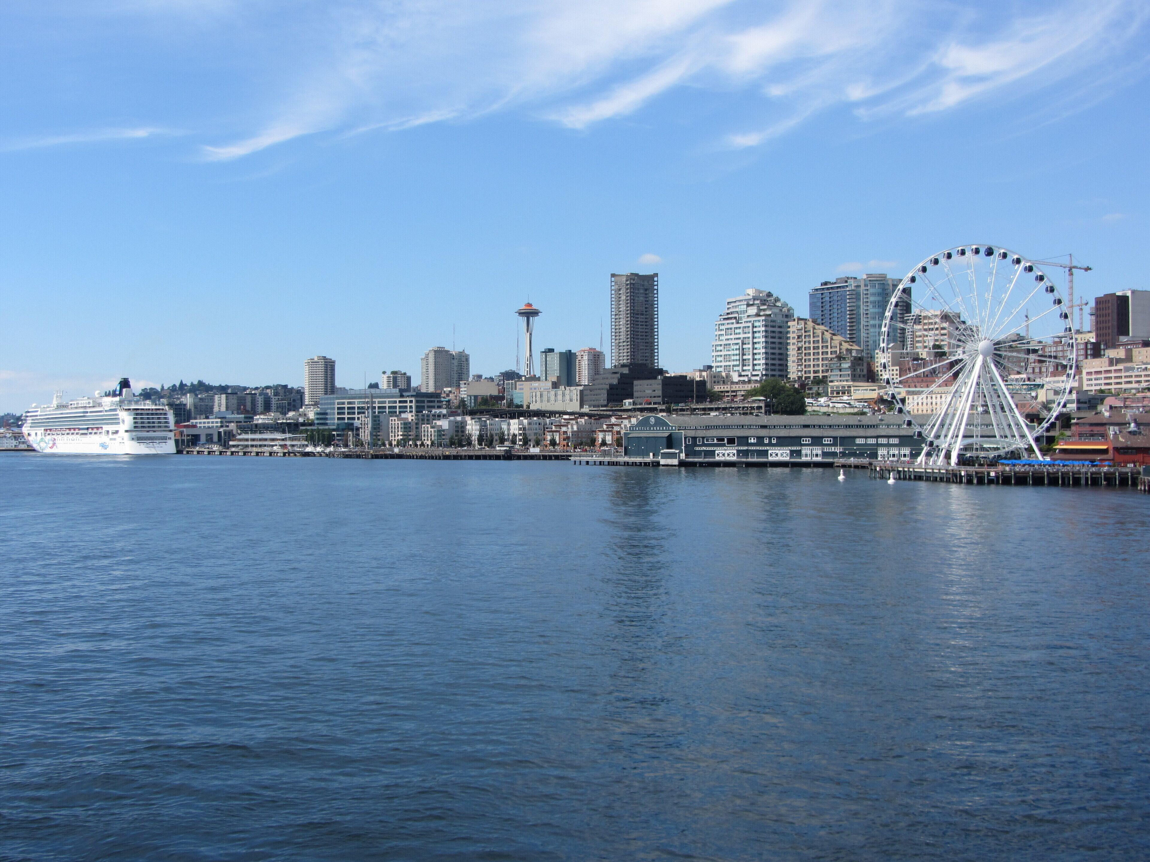 Une vue sur la ville, avec ses bâtiments donnant sur le front de mer, un navire de croisière amarré, une grande roue et la Space Needle.