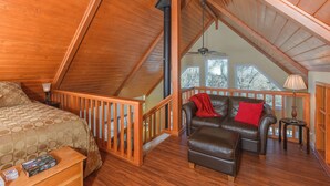 A cozy attic bedroom with a wooden ceiling, a bed, a leather sofa, and a nightstand. - Cozy Cottage Retreat,  Close to Yosemite, Beautiful Views, Hot Tub & More! (Mariposa)