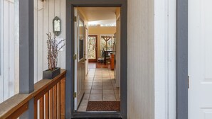 A hallway with a wooden railing, a potted plant, and a door leading to a room with a tiled floor and a bench. - Cozy Cottage Retreat,  Close to Yosemite, Beautiful Views, Hot Tub & More! (Mariposa)