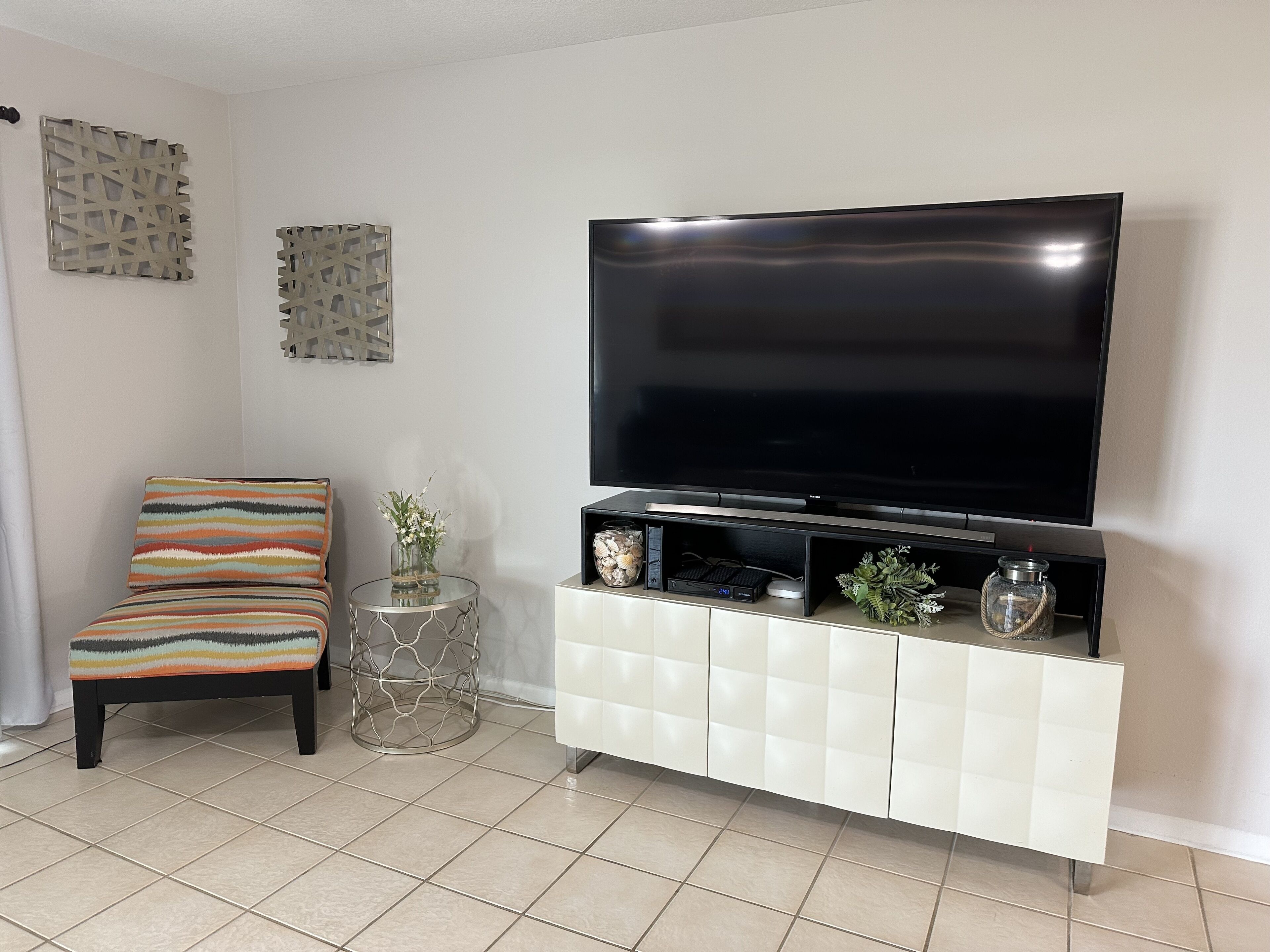 Een woonkamer met een flatscreen televisie, een bank, een bijzettafeltje met decoratieve objecten, en een witte kast.