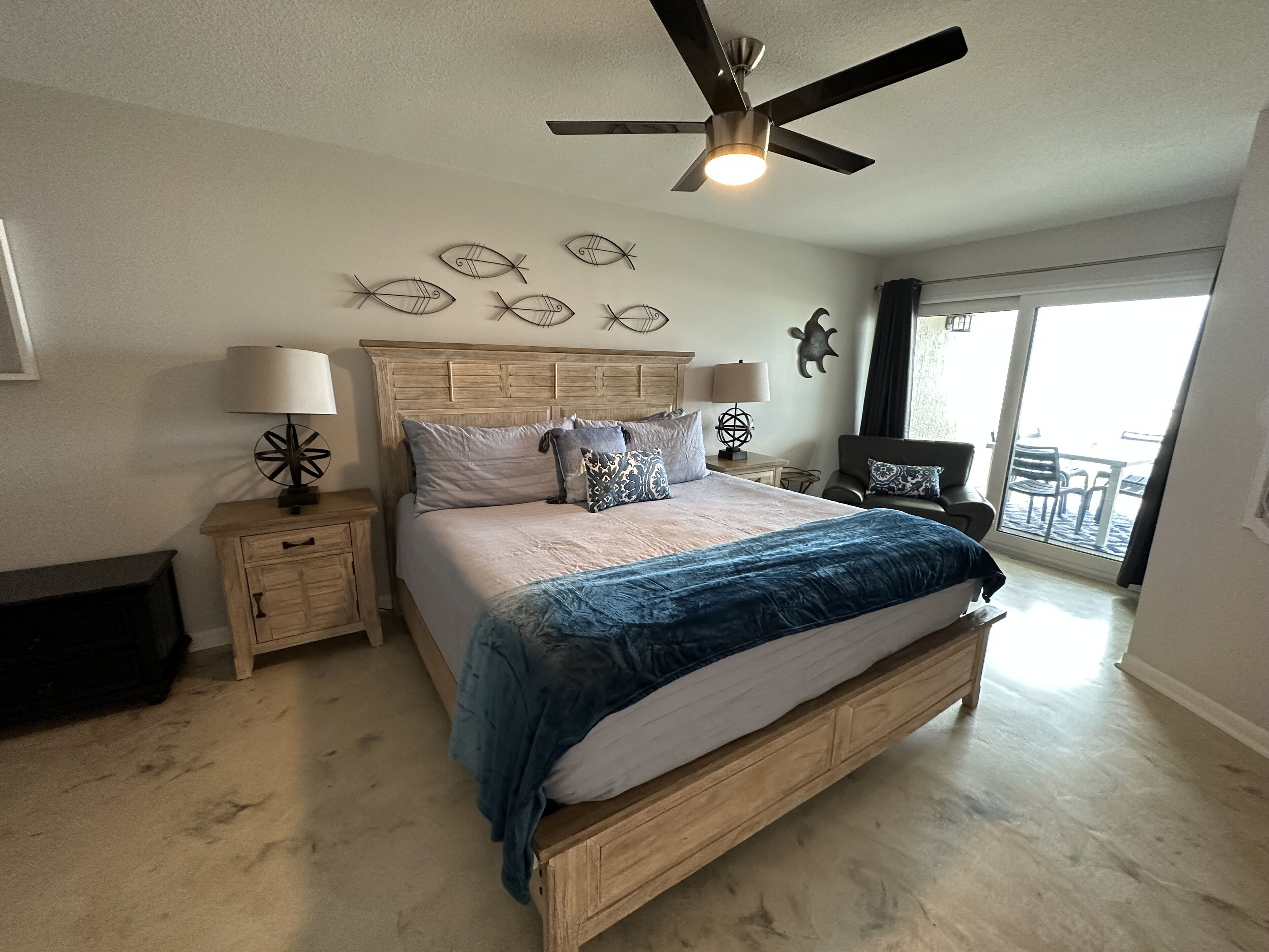 Ein Schlafzimmer mit Bett, Nachttischen, Deckenventilator, Wanddekoration und Blick ins Freie.