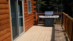 A wooden cabin with a deck, a sliding glass door, and a barbecue grill.
