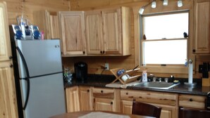 A wooden cabin kitchen with a refrigerator, stove, sink, and dining table with chairs.