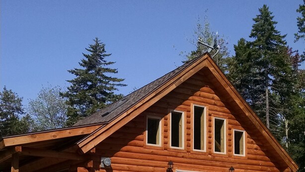A log cabin with a wooden deck, a covered porch, and a gravel driveway.