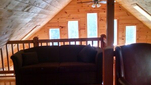 An attic room with wooden flooring, a sofa, a chair, and a ceiling fan.