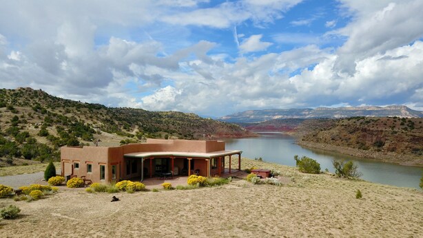 A house with a patio overlooking a lake, surrounded by hills and sparse vegetation. - Stellar, Southwest, Luxury home.  Extraordinary location on Abiquiu Lake (Gallina)