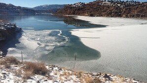 A frozen lake with clear water, surrounded by snow-covered ground and rocky terrain. - Stellar, Southwest, Luxury home.  Extraordinary location on Abiquiu Lake (Gallina)