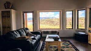 A living room with a leather couch, a small wooden table, and a view of a natural landscape through large windows. - Stellar, Southwest, Luxury home.  Extraordinary location on Abiquiu Lake (Gallina)
