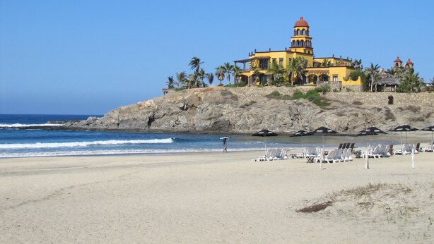 A coastal building with a tower, surrounded by palm trees and beach chairs. - Puesta Del Sol Top Unit 2BR Condo Private Rooftop+ Steps to Cerritos Surf Beach (Cerritos Beach)