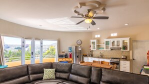 A modern living room with a leather sectional sofa, a ceiling fan, and a view of a kitchen and balcony. - Puesta Del Sol Top Unit 2BR Condo Private Rooftop+ Steps to Cerritos Surf Beach (Cerritos Beach)