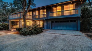 A two-story house with a covered porch, a garage, and a gravel driveway. - Peek of Blue – 2nd Row Sea Pines Home, Pool & Spa, Sleeps 17, 800 Ft to Beach (Hilton Head Island)