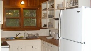 Une cuisine compacte avec des meubles blancs, un réfrigérateur à deux portes et un plan de travail en bois.