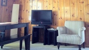 Une pièce aux murs lambrissés, avec un téléviseur posé sur un meuble, un fauteuil à rayures et une petite table.