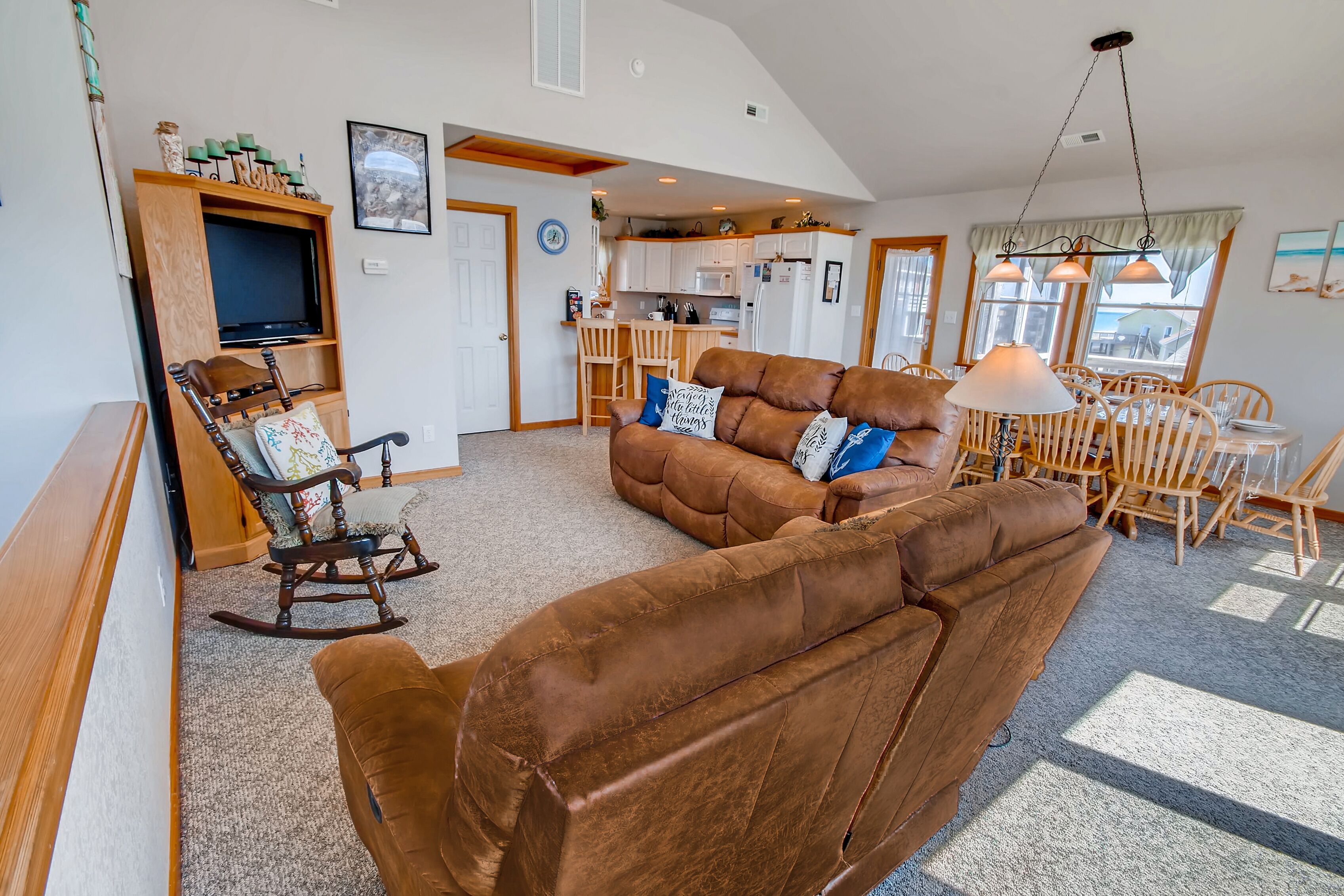 A spacious living room with a brown leather sofa, a wooden rocking chair, and a television on a wooden shelf.