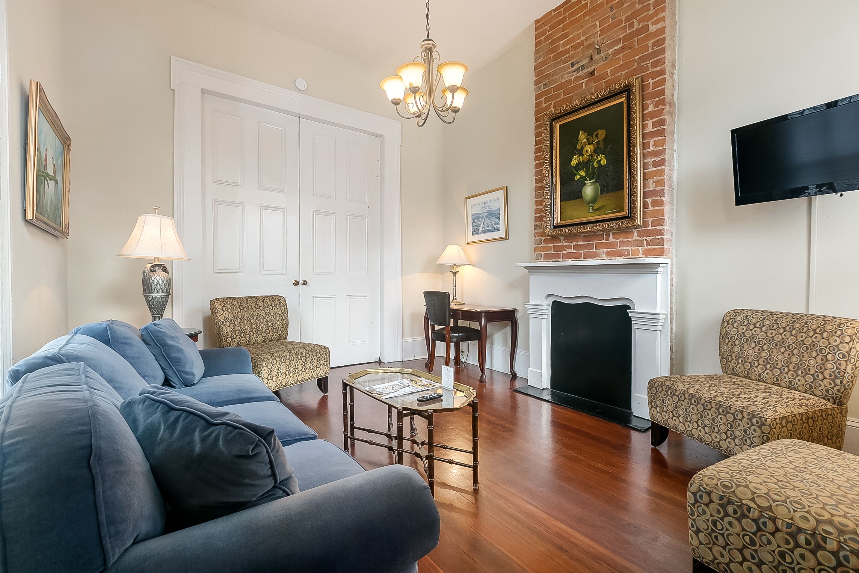 A living room with a blue sofa, patterned armchairs, a small table, a fireplace, and a TV mounted on the wall.