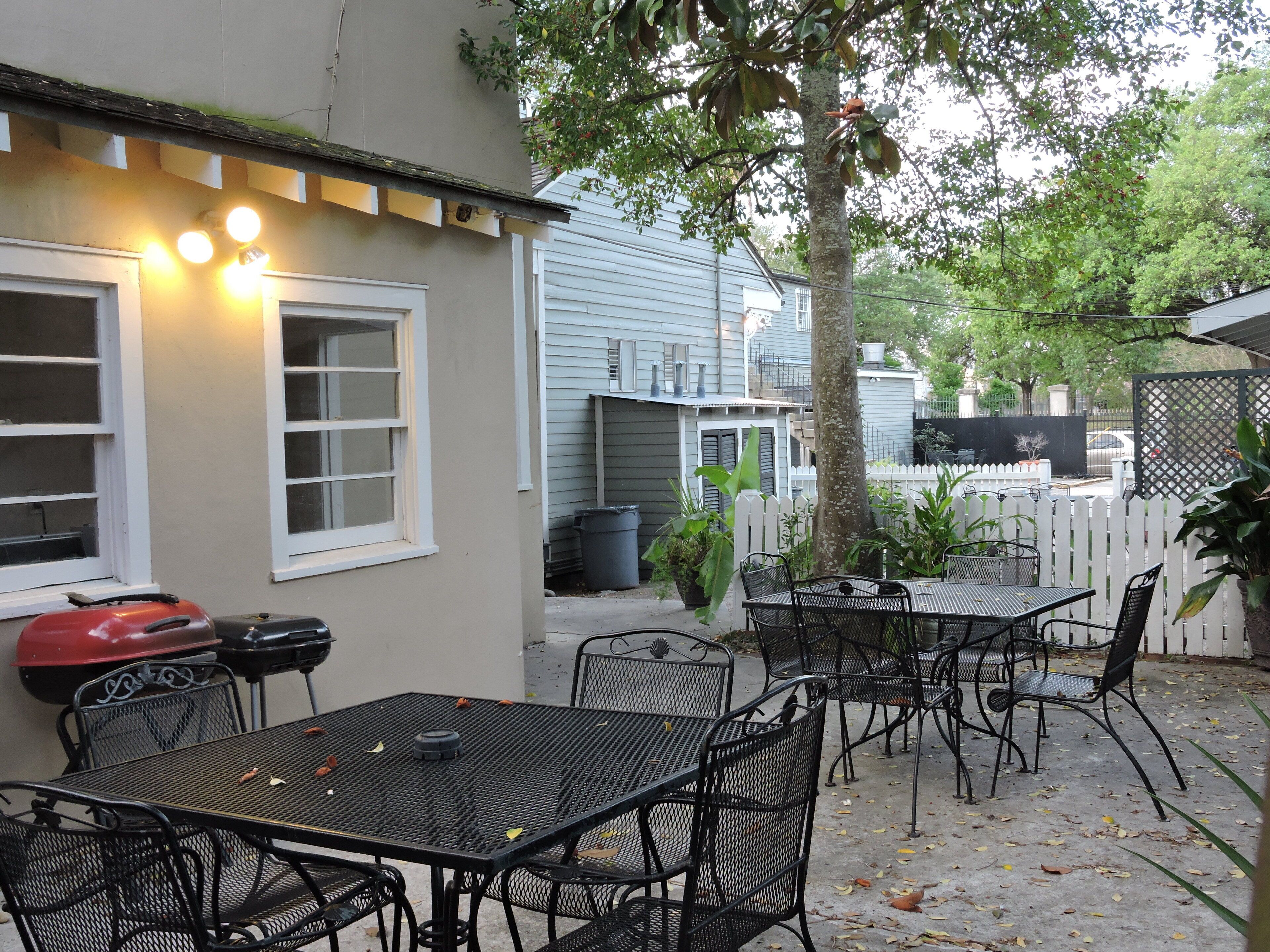 Eine Außenpatio-Terrasse mit Metalltischen und -stühlen, einem Grill und einem weißen Zierzaun.
