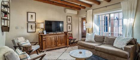Un salón acogedor con techo de madera, televisor y un amplio ventanal con cortinas.
