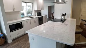 Una cocina moderna con armarios blancos, una encimera de mármol grande y un lavavajillas integrado.