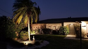 Una casa residencial con jardín cuidado, una palmera y un coche aparcado.