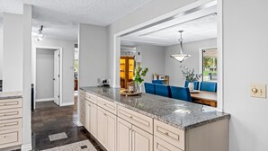 A modern kitchen with a granite countertop, beige cabinetry, and a dining area with blue chairs and a table.