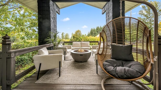A covered outdoor patio with a fire pit, seating area, and a view of the surrounding greenery.
