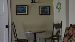 Un comedor con dos sillas de madera y una mesa redonda, un aplique de pared y dos cuadros enmarcados que muestran pájaros y paisajes acuáticos.
