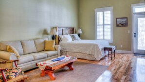 Una habitación con sofá, cama, una mesita de madera y una pequeña mesa con l ámparas.