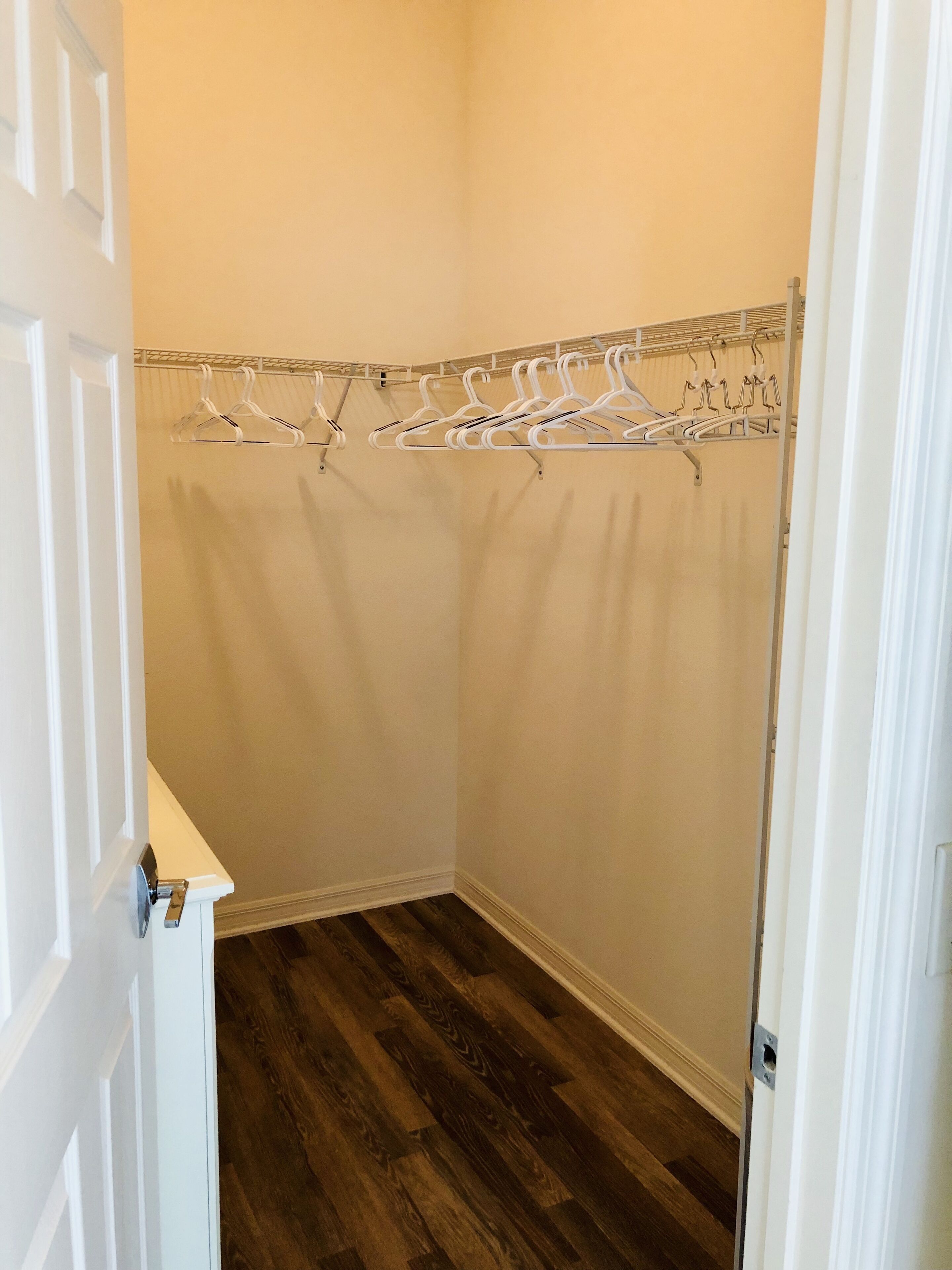 Un placard d’angle avec un plancher en bois, une porte blanche et un étendoir métallique muni de plusieurs supports à cintres.
