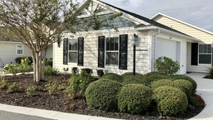 Une maison de plain-pied avec un toit à pignon, des volets noirs et un porche à l’avant.