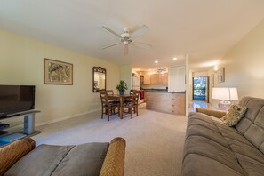 A living room with a television, a sofa, a dining table with chairs, and a ceiling fan. - Turtle Bay resort, Prime location, 18th hole   (Kahuku)
