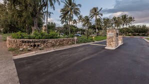 A gated entrance with a stone wall, palm trees, and a clear sky. - Turtle Bay resort, Prime location, 18th hole   (Kahuku)