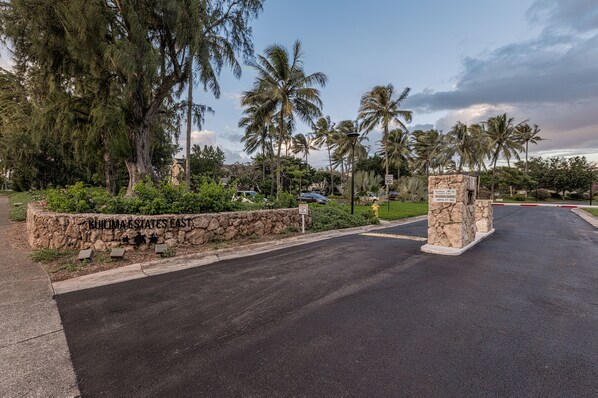 A gated entrance to a residential area with a stone wall, palm trees, and a speed limit sign. - Turtle Bay resort, Prime location, 18th hole   (Kahuku)