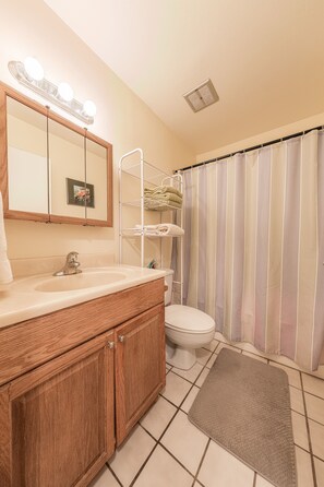 A bathroom with a wooden vanity, a sink, a mirror with lights, a toilet, and a striped shower curtain. - Turtle Bay resort, Prime location, 18th hole   (Kahuku)