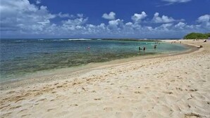 A sandy beach with clear turquoise water and a few people in the distance. - Turtle Bay resort, Prime location, 18th hole   (Kahuku)