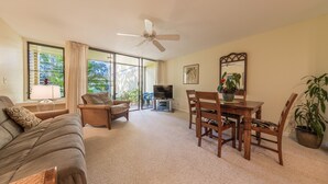 A living room with a sofa, two armchairs, a dining table with chairs, a ceiling fan, a television, and a large window with curtains. - Turtle Bay resort, Prime location, 18th hole   (Kahuku)