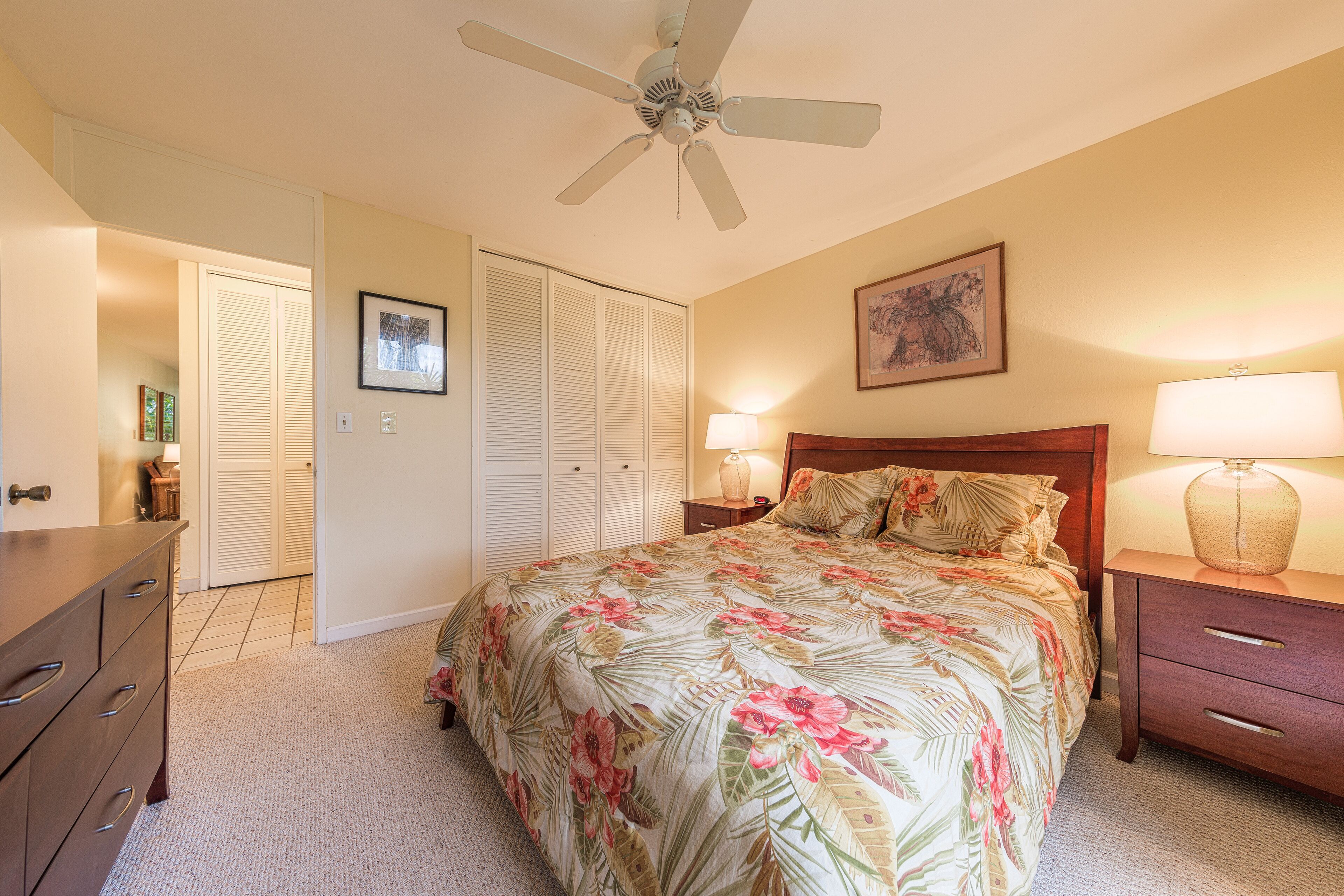 A bedroom with a bed, a nightstand, a dresser, a ceiling fan, and a door leading to a closet.