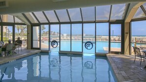 Una piscina interna con vista diretta sulla spiaggia e sull'oceano attraverso ampie finestre.