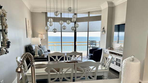Una cucina moderna con un piano di lavoro in marmo, un'area pranzo con sedie bianche e vista sull'oceano attraverso ampie finestre.