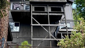 Une cabane en bois à plusieurs étages, dotée d’un balcon et entourée d’arbres et d’une clôture.