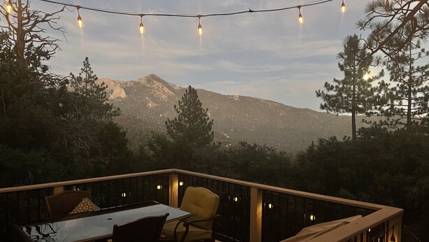 Une terrasse extérieure avec une table et des chaises, des guirlandes lumineuses et une vue imprenable sur les montagnes.