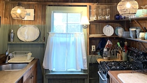 Una cocina rústica con vigas de madera, una lámpara colgante y un ventanal con cortinas.