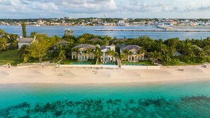 A beachfront property with a swimming pool, a large house, and a view of the ocean and city skyline. - On Beach Time |Lux Villa|Oceanfront|Heated Pool (Nassau)