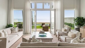 A spacious living room with a large window offering a view of the ocean and a patio area. - On Beach Time |Lux Villa|Oceanfront|Heated Pool (Nassau)