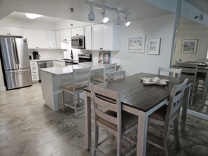 A modern kitchen with white cabinetry, stainless steel appliances, and a wooden dining table.