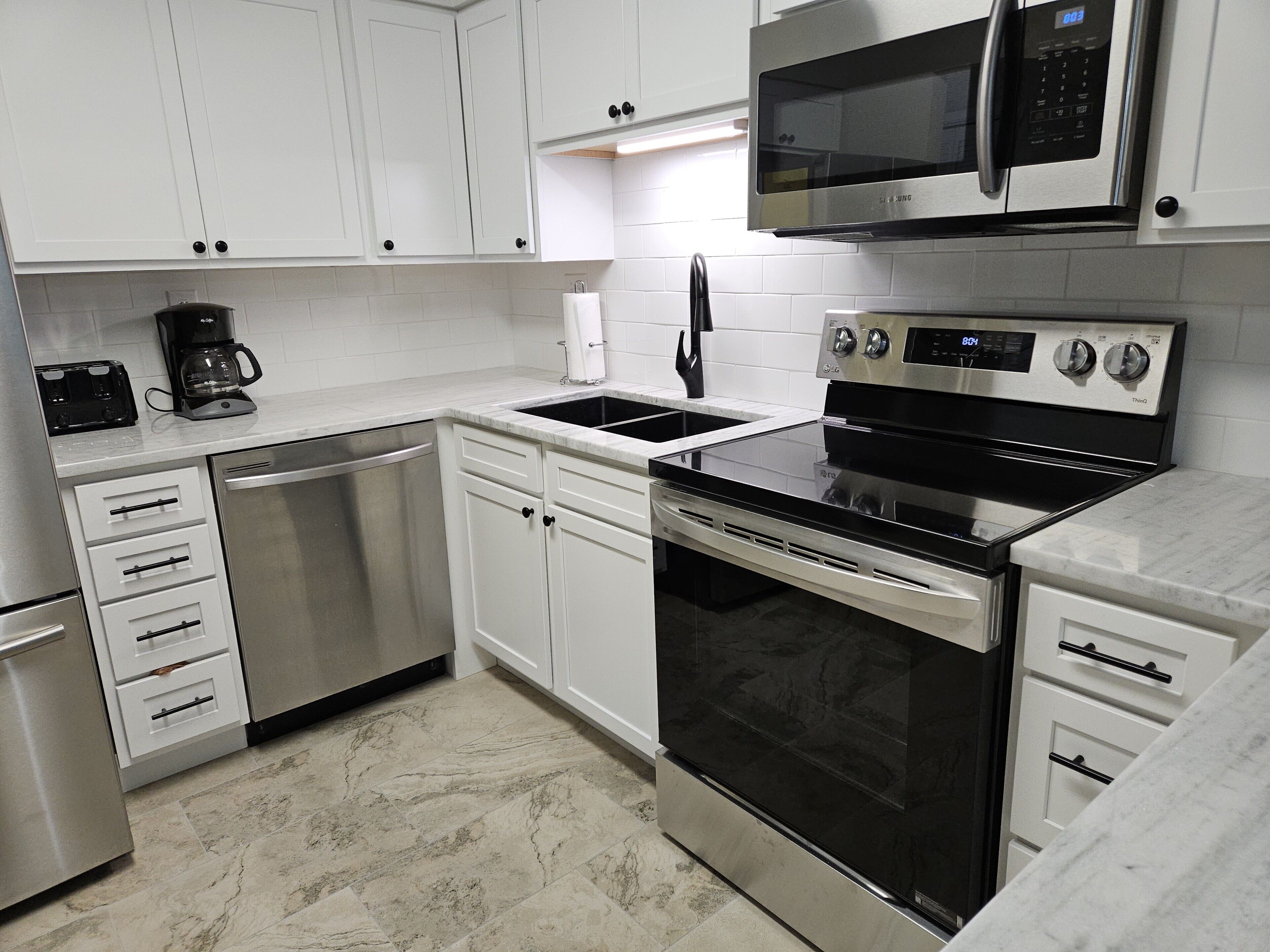Una cucina moderna con elettrodomestici in acciaio inossidabile, mobili bianchi e una parete backsplash rivestita di piastrelle.