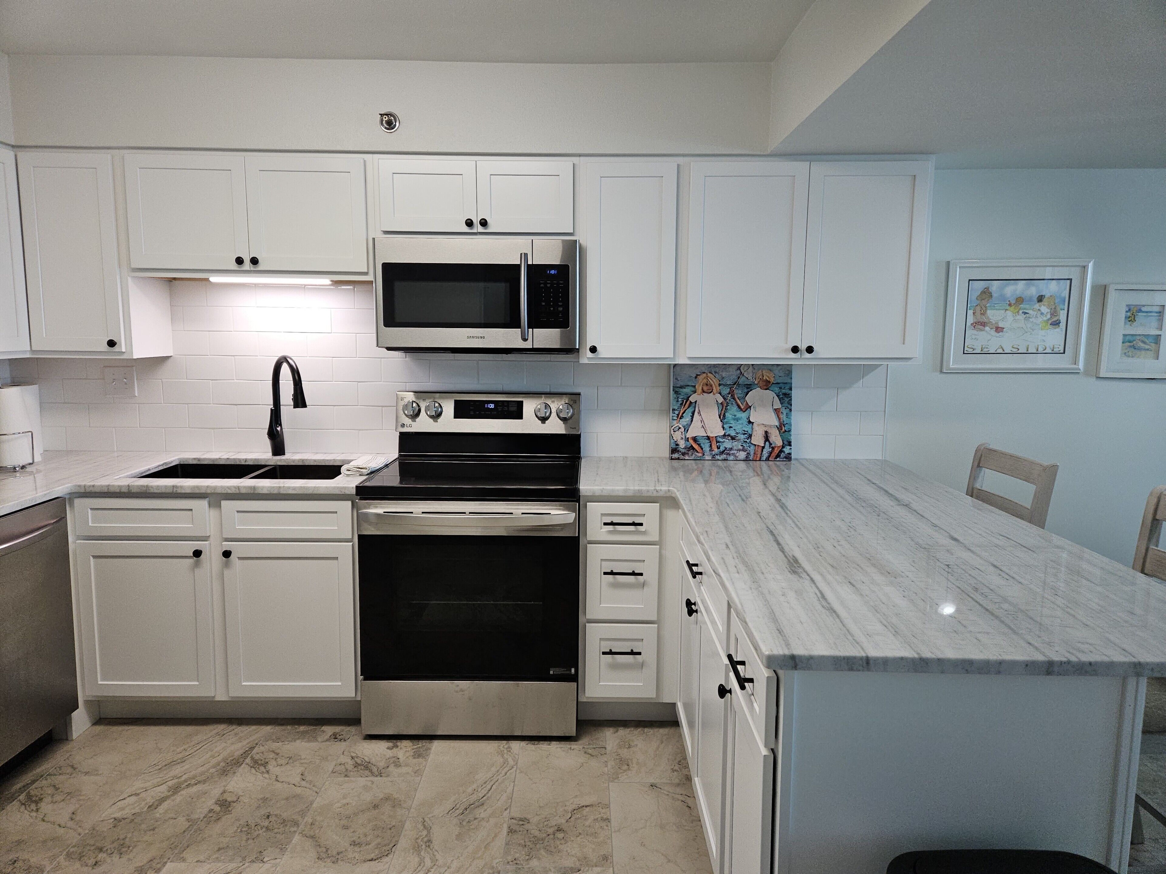 A modern kitchen with white cabinets, stainless steel appliances, and a marble countertop.