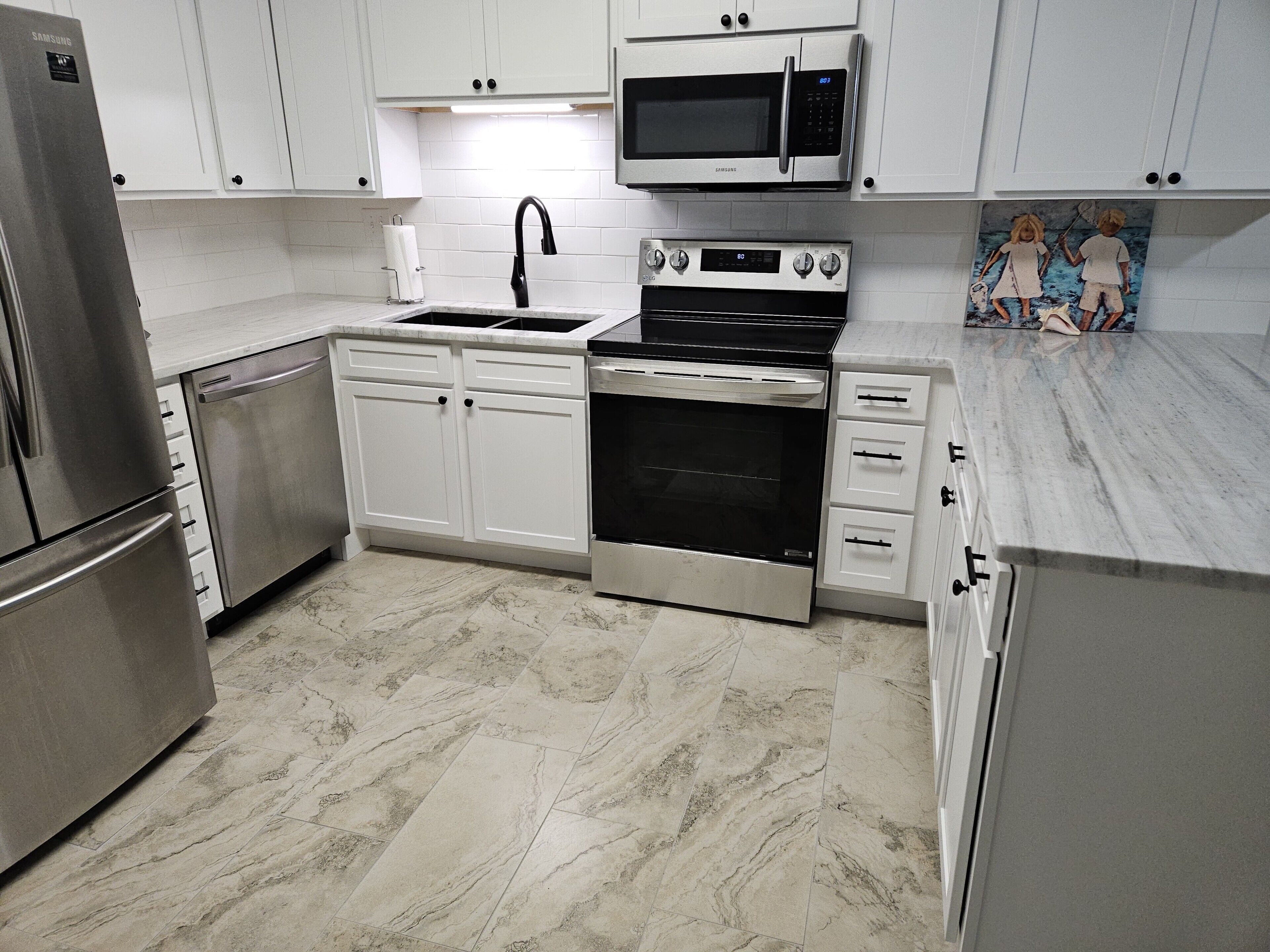 A modern kitchen with stainless steel appliances, white cabinetry, and a marble floor.