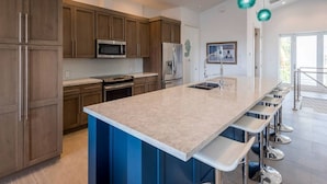 A modern kitchen with a large island, stainless steel appliances, and blue bar stools. - Grouper House: 4 Masters/6 BA, Pool/Dock, BoatRamp (Marathon)